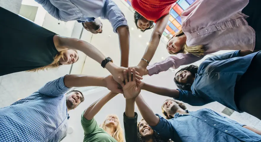 Une équipe diverse célèbre une réussite lors d'une activité de groupe, mains jointes au centre.