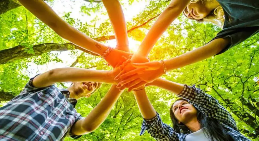 Des mains s'unissent dans un cercle, symbolisant un jeu ludique adulte en pleine nature.