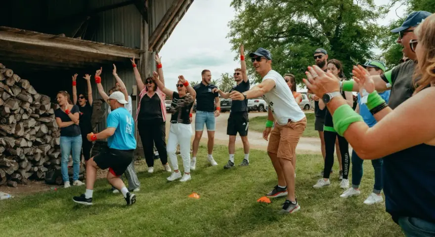 Des participants enthousiastes s'amusent lors d'un événement de team building jeux olympiques, bras levés et souriants.