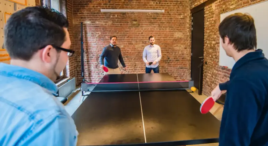 Des hommes jouent au ping-pong, une activité de jeux d'intérieur en groupe, dans un bureau moderne avec des murs en briques.