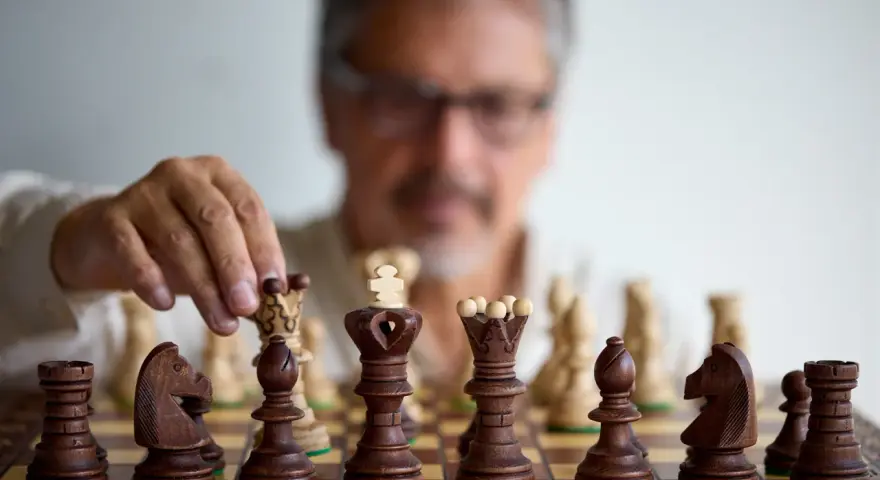 Un homme réfléchit, une pièce d'échecs à la main. Il faut avoir un esprit critique pour anticiper chaque mouvement.