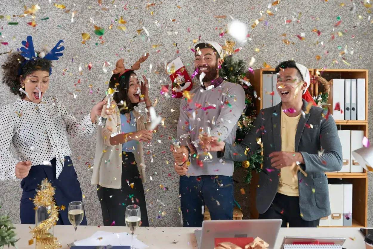 Des collègues célèbrent joyeusement les jeux de noël entre collègues avec des confettis et des coupes de champagne.
