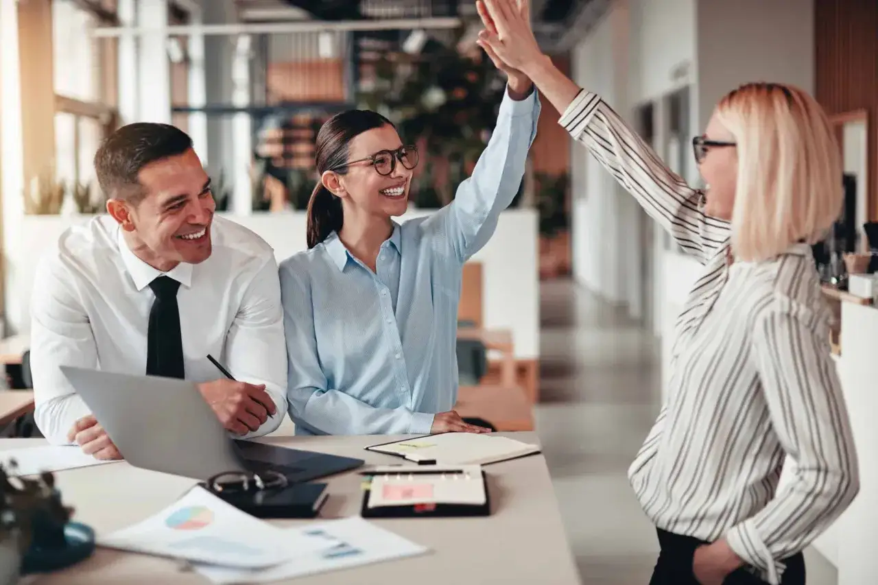 Trois coll&egrave;gues c&eacute;l&egrave;brent un succ&egrave;s. La reconnaissance au travail est palpable dans leurs sourires et leur high five.