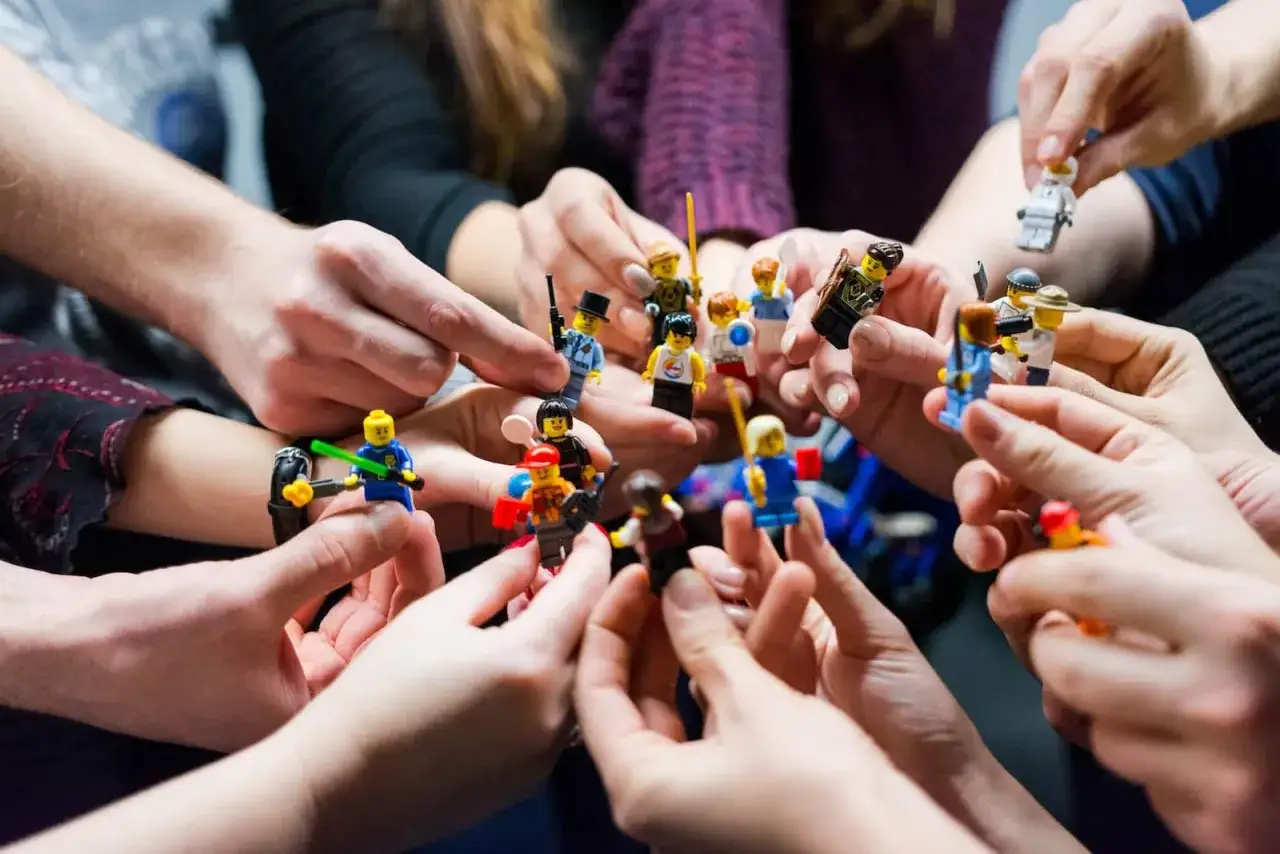 Des mains tiennent des figurines Lego, cr&eacute;ant une sc&egrave;ne de jeux d'int&eacute;rieur en groupe.