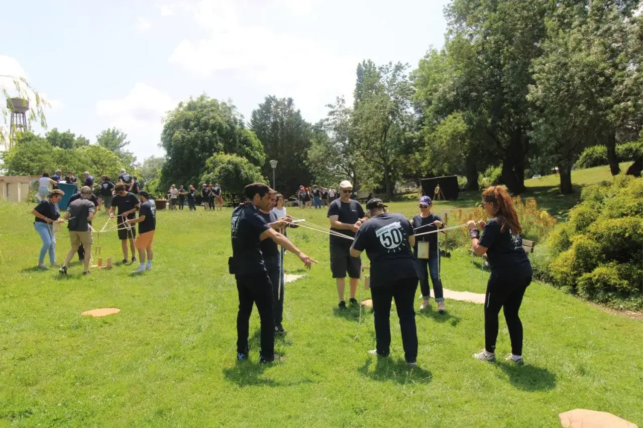 Des participants s'amusent lors d'une activit&eacute; team building plein air, manipulant des cordes et des blocs de bois dans un parc verdoyant.