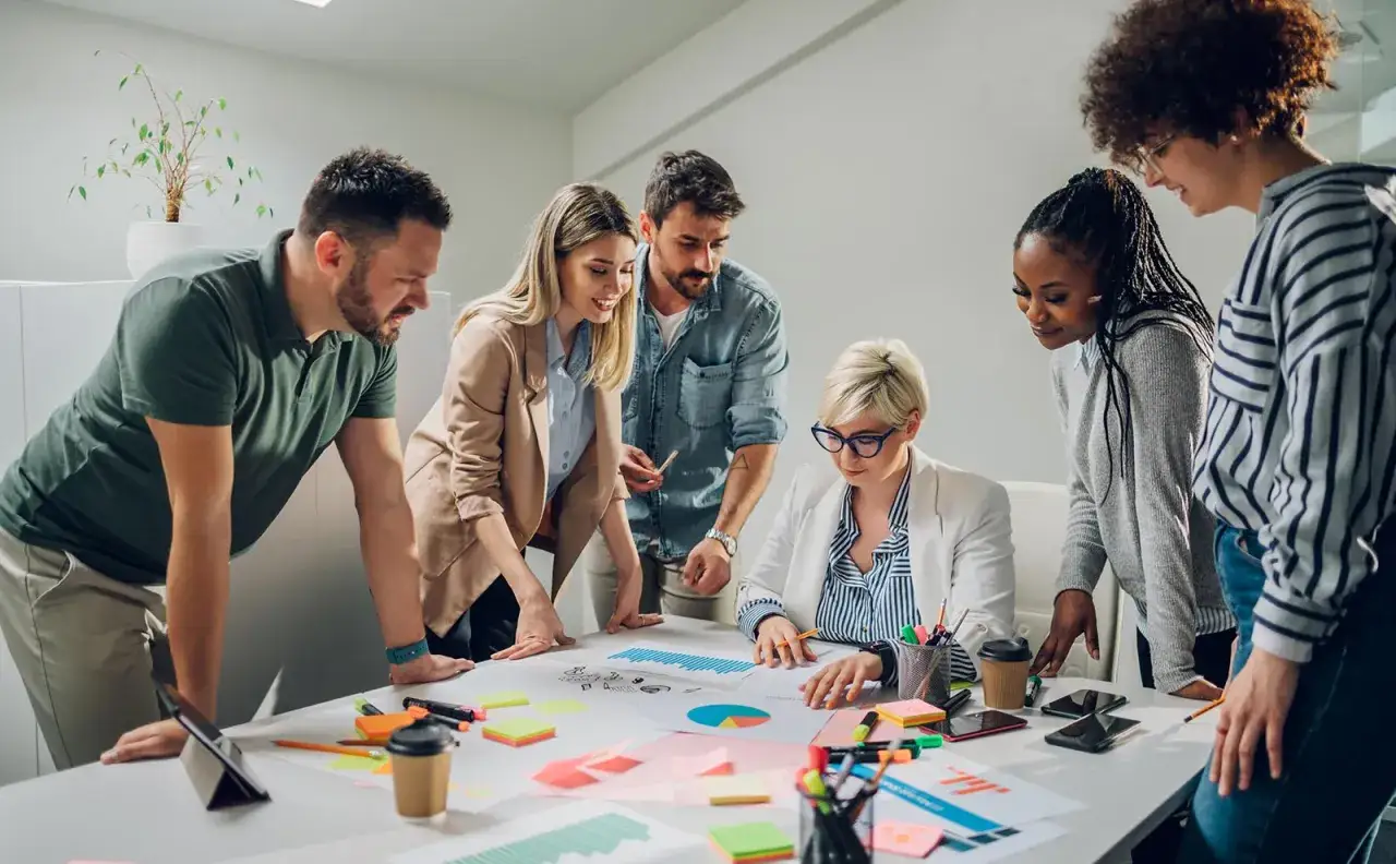 Une &eacute;quipe diversifi&eacute;e discute de graphiques et de notes adh&eacute;sives, illustrant la solidarit&eacute; au travail.