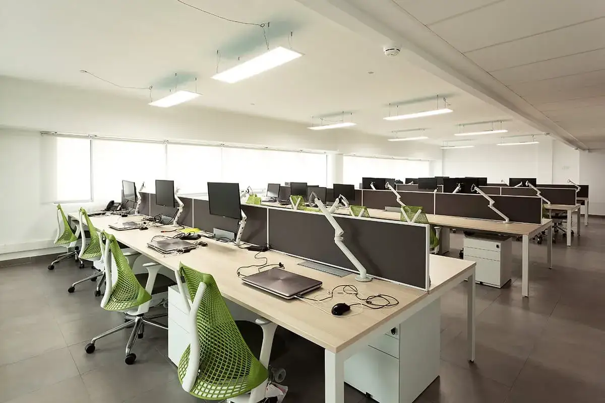 Bureau moderne et lumineux, prêt pour le digital workplace. Rangées de postes de travail avec écrans, chaises vertes vives et cloisons grises.