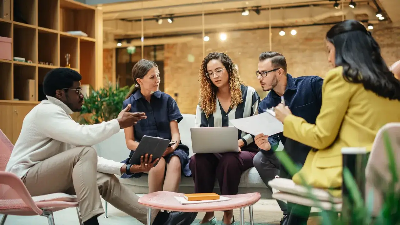 Une &eacute;quipe discute autour d'un ordinateur portable, illustrant la plateforme collaborative d&eacute;finition et le travail d'&eacute;quipe moderne.