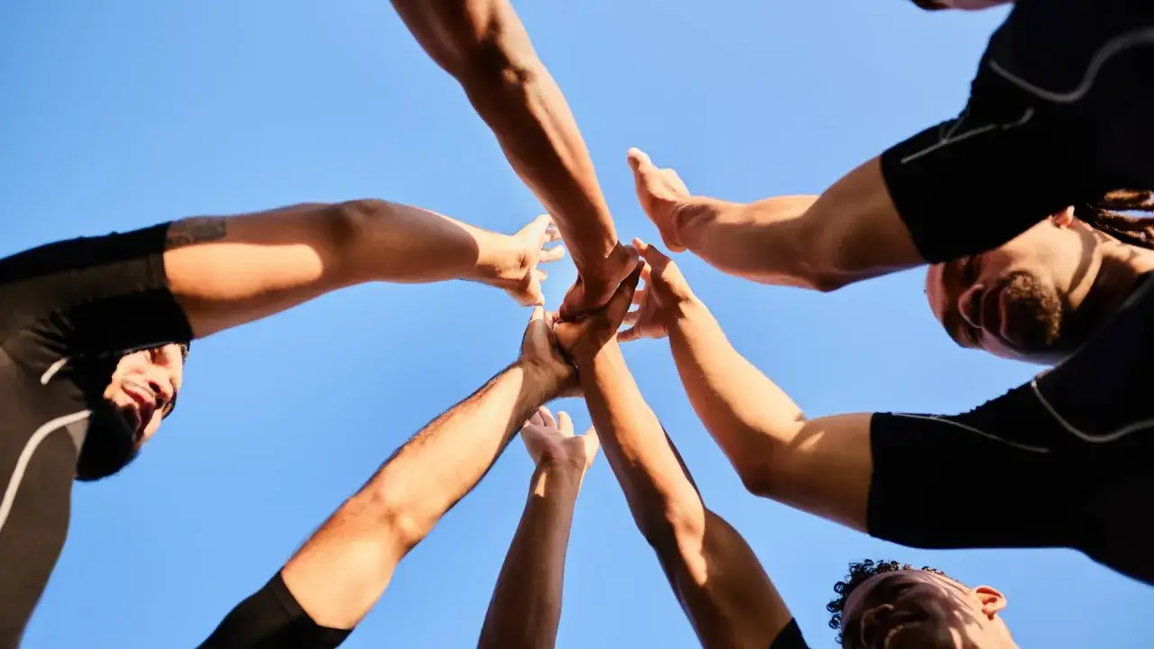 Des mains se rejoignent sous un ciel bleu, symbolisant une id&eacute;e de challenge sportif et l'esprit d'&eacute;quipe.