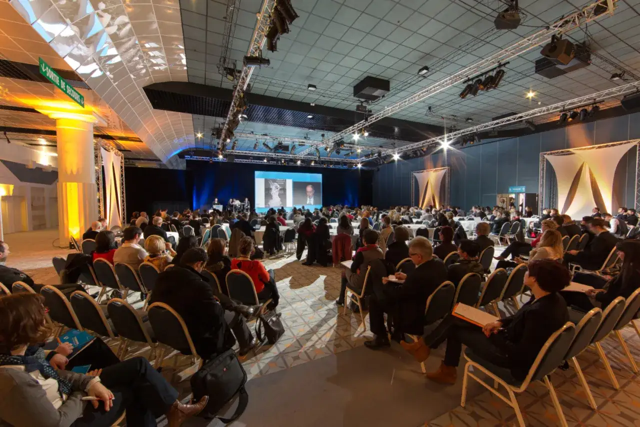 Salle de conférence avec public attentif. Un écran projette des images. Idéal pour un week-end entreprise réussi.