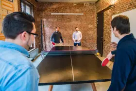 Des hommes jouent au ping-pong, une activité de jeux d'intérieur en groupe, dans un bureau moderne avec des murs en briques.