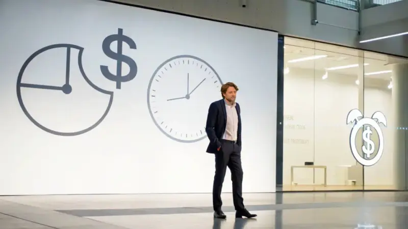 Un homme en costume présente une conférence pecha kucha. Des horloges et un symbole dollar sur l'écran suggèrent le thème du temps et de l'argent.